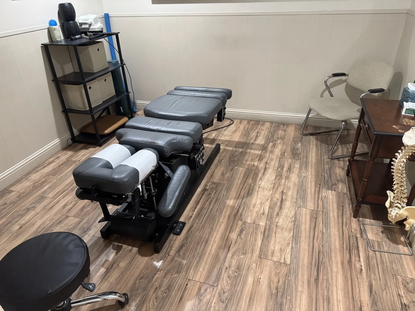 Adjustment room at the Manteca office with a grey chiropractic drop table, therapy tools, and a spine model