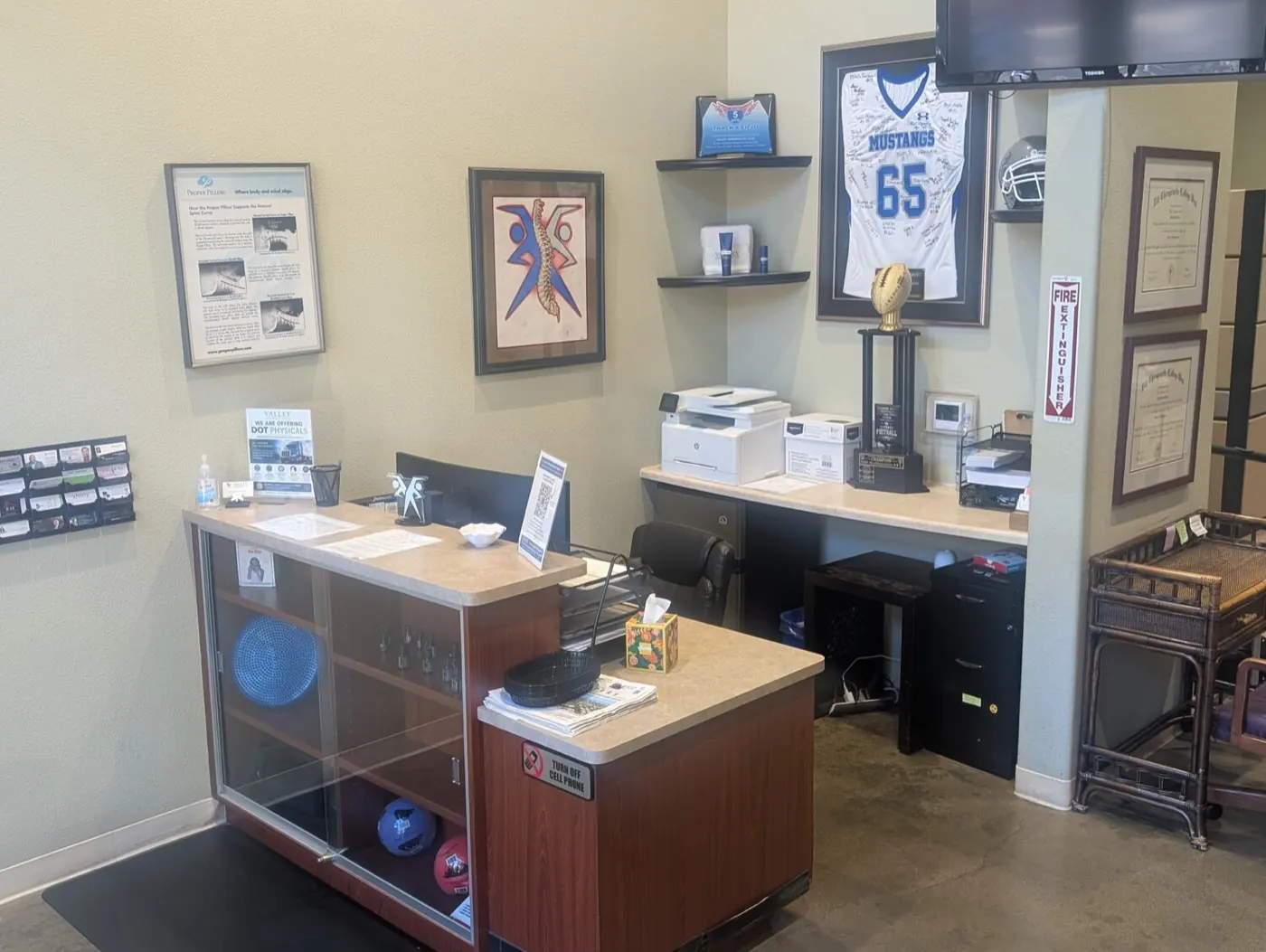 Front desk at the Mountain House chiropractic office, with a signed Mustangs football jersey and team trophy on the wall behind it