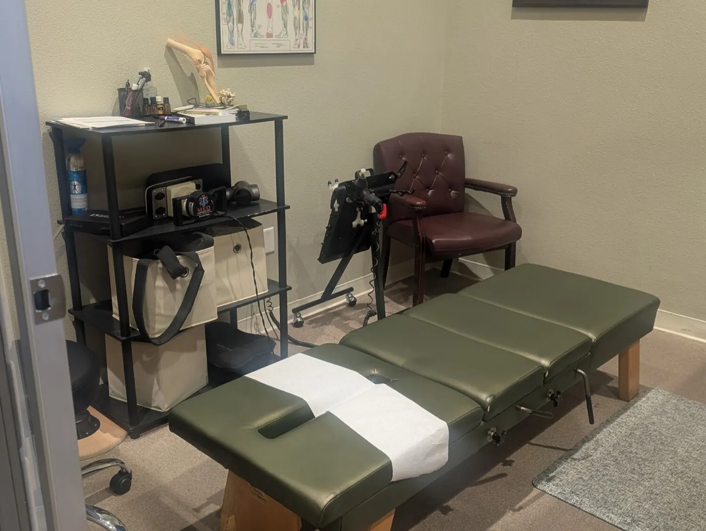 Adjustment room at the Mountain House office with a green chiropractic table, therapy equipment cart, and anatomy chart