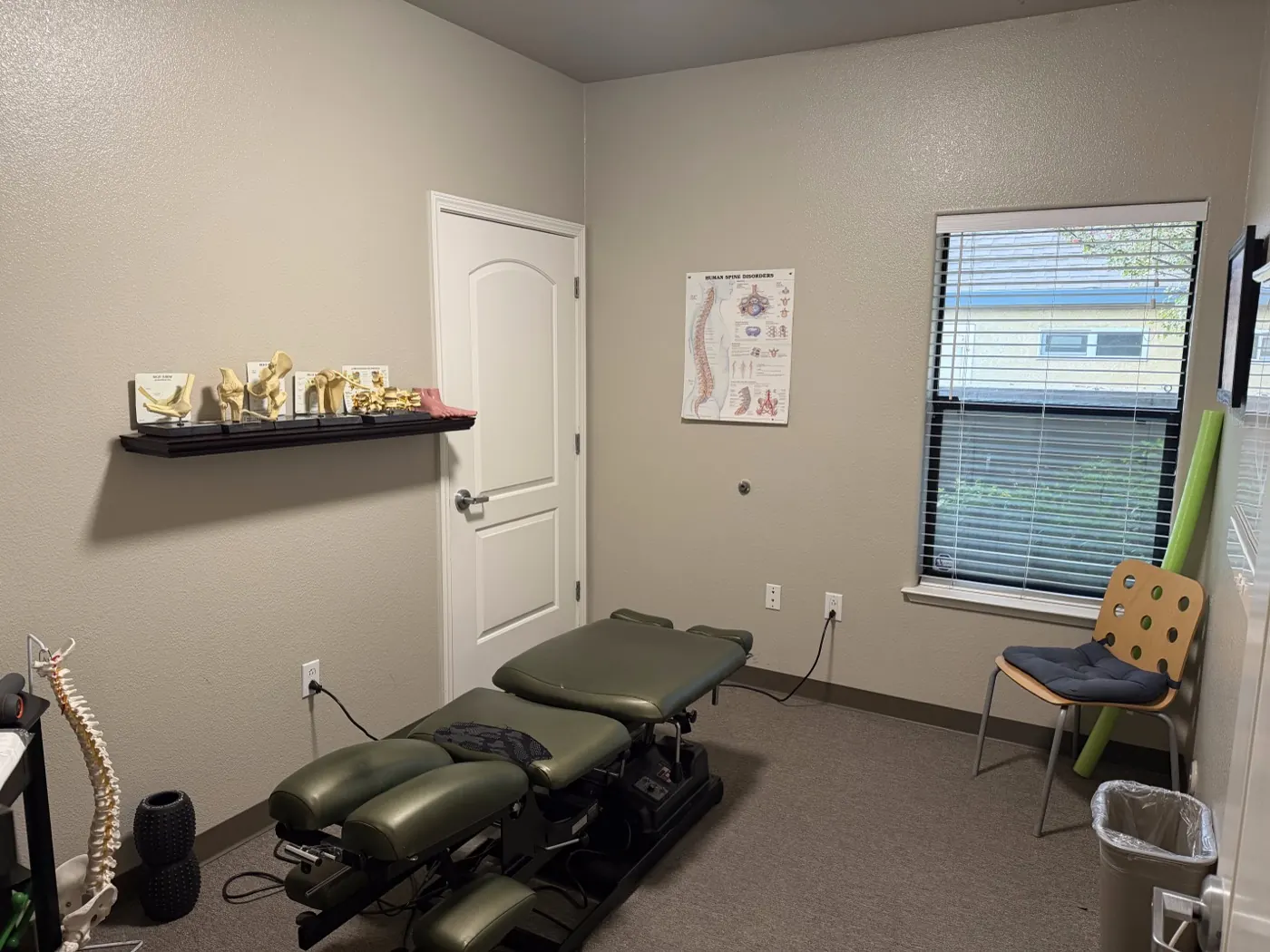 Chiropractic adjustment room in Tracy with a green drop table, spine and joint models, and a human spine disorders chart